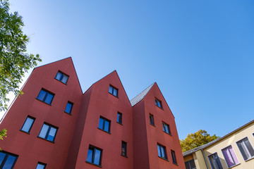 Outdoor view of typical style building with contemporary modern gamble roof, simple rectangular windows and red exterior facade, in europe. 