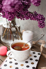Romantic background with cup of tea, lilac flowers and macaroons. A bouquet of lilac in a vase. Floral card for Mothers or Womans Day