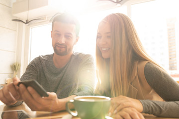 Pretty young woman and her boyfriend looking through online stuff in smartphone