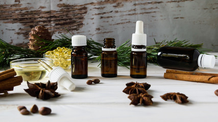 composition of natural oils, glass bottles with oil, cinnamon sticks, anise, pine nuts on a white...