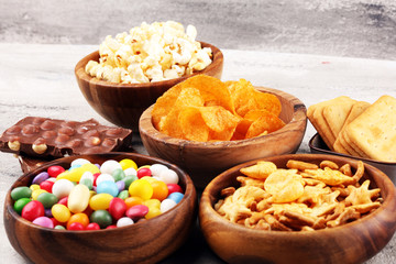 Salty snacks. Pretzels, chips, crackers in wooden bowls and candy and chocolate on table