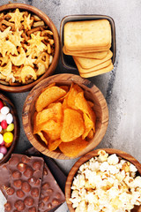 Salty snacks. Pretzels, chips, crackers in wooden bowls and candy and chocolate on table