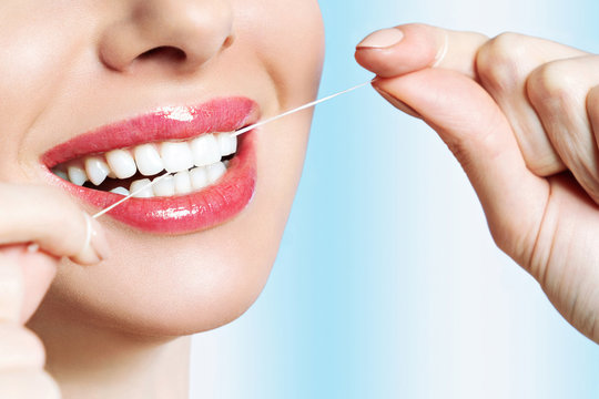 Young beautiful woman is engaged in cleaning teeth. Beautiful smile healthy white teeth. A girl holds a dental floss. The concept of oral hygiene. Promotional image for a dental clinic