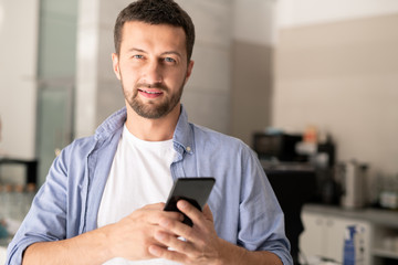 Young confident businessman in casualwear scrolling in smartphone