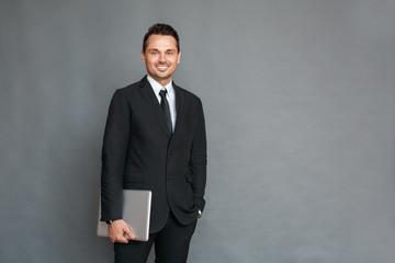 Businessman studio standing isolated on grey with laptop looking camera cheerful