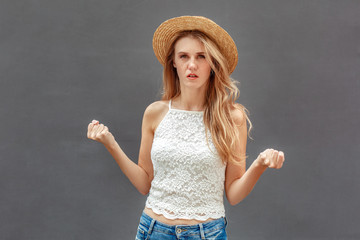 Freestyle. Young woman in hat standing isolated on wall hands in fists looking camera angry