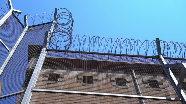wall of the prison building with small windows with bars and a high fence