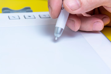 Designer hand with a digital pen on a white tablet in the process of work. Close-up. Copy space.