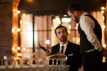 Portrait of mature bearded businessman talking to waiter while ordering dinner in luxury restaurant, copy space