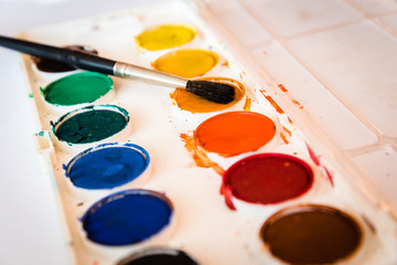 The palette of watercolor paint and one brush on white sheets of paper