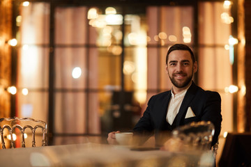 Portrait of handsome gentleman looking at camera and smiling while sitting at table in luxury restaurant