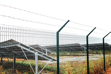 Solar panel or photovoltaic farm behind metal chainlink fence on green field with dramatic cloudy...