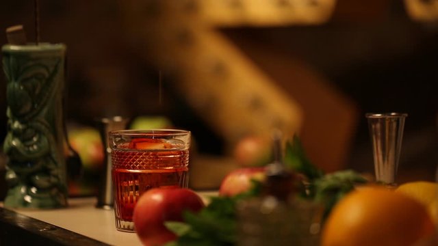 The bartender pours an alcoholic drink into a glass with ice in a thin stream