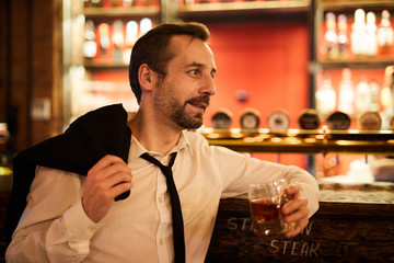 Side view portrait of bearded mature businessman drinking whiskey while relaxing in bar after work