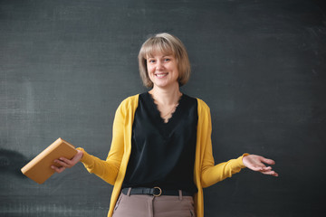 Young teacher standing near blackboard in a classroom and is shrugging her shoulders.