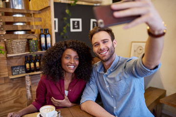 Diverse young couple smiling while taking selfies in a cafe