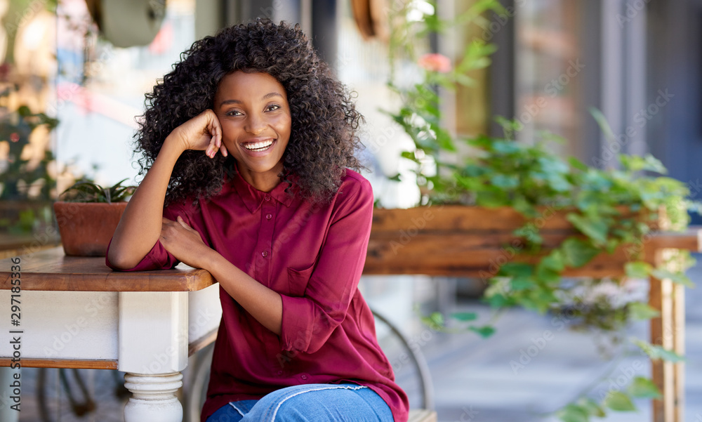 Wall mural smiling young african american woman sitting outside of her cafe