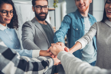 Obraz premium Startupers working at office together standing holding hands close-up smiling joyful