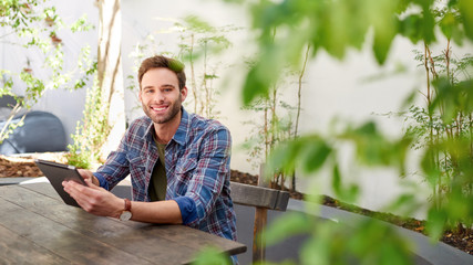 Smiling young man sitting sitting outside using a digital tablet