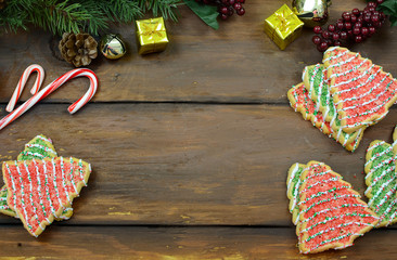 Christmas tree shaped sugar cookies, candy canes pine branches with cones, mini gifts and jingle bells on a wide-plank rustic wooden background. Copy space