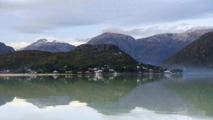 Panoramic view from the sea of Caleta Tortel in Patagonia Chile. You see some houses and boats reflected in the water, as well as the great mountains of the place