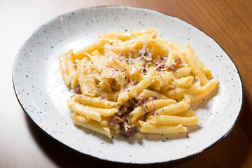 Penne pasta in cheese sauce with bacon on a wooden background