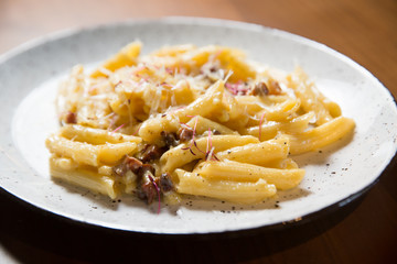 Penne pasta in cheese sauce with bacon on a wooden background