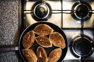 Fried pies in a pan standing on a gas stove, top view