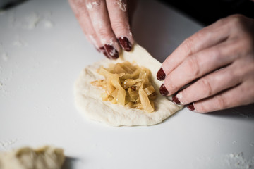 Modeling a pie on a white table with female hands, flour, fried cabbage
