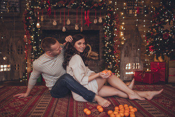 Lovely couple woman and man are lying at home with mandarins. Xmas time.