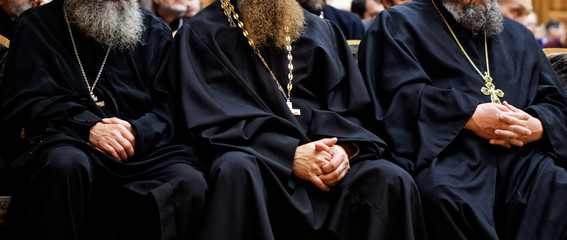 Three Christian priests in robes, with beards and crosses are sitting at a meeting