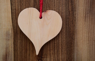 Helles Holzherz mit roter Schleife auf dunklen Holzhintergrund - Symbol für die Liebe