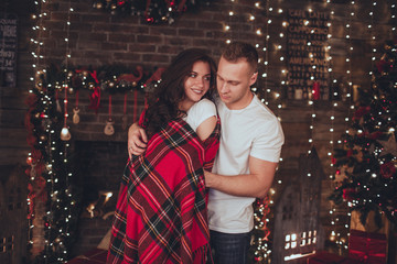 Fototapeta premium Lovely couple woman and man are covered in blanket at home near fireplace. Christmas time.