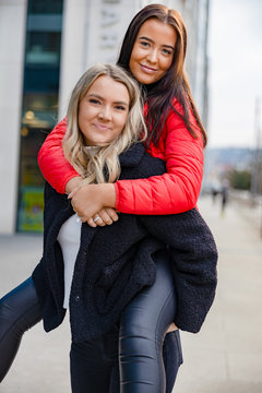 Smiling Woman Piggybacking Female Friend In City