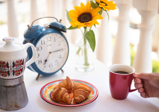 Breakfast on the table. Close up on the fresh croissants. Hands of a senior woman holding a cup of coffee. Coffee time outdoor in the terrace. Beautiful  yellow sunflowers