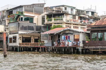 Fototapeta na wymiar Bangkok city, Thailand - March 17, 2019: Chao Phraya River. Laundry at poor dwelling built on stilts just above the water with better and more expensive housing as neighbors.