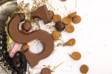 Broken Sinterklaas chocolate letter S at shoe surrounded with gingerbread cookies, sweets and hay residues.