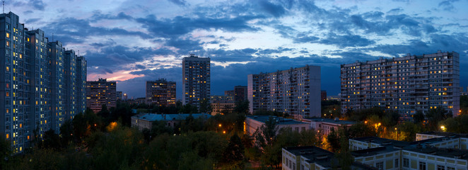 Cityscape, evening city lights with dramatic cloudy sunset sky on background, residential district of town, panoramic view 