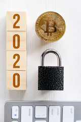 Bitcoin with numbers 2020 on cubes on a white keyboard wooden background a lock. Cryptocurrency security concept in the new year. Flat lay. Copy space.