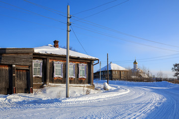 Snow-covered village street with old wooden residential houses. Village of Visim, Ural, Sverdlovsk region, Russia