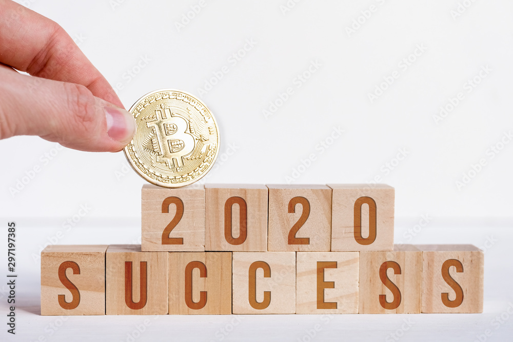 Sticker Bitcoin with 2020 numbers on cubes on a white wooden background with the letters success. The concept of success and popularity in the new year of cryptocurrency.