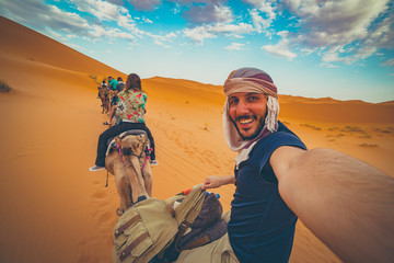 happy nomad man taking crazy selfie during camel riding in Sahara Desert, Merzouga, Morocco - obrazy, fototapety, plakaty