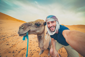 happy nomad man taking crazy selfie during camel riding in Sahara Desert, Merzouga, Morocco