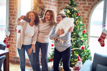 Middle age women smiling happy and confident. Standing holding dog make selfie by smartphone around christmas tree