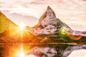 Matterhorn mountain peak, Switzerland, seasonal autumnal scene. Epic sunset view on Matterhorn mountain peak in Switzerland over Riffelsee lake. Sun glowing during sunset. Swiss mountain landscape. - obrazy, fototapety, plakaty