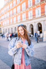 Portrait of stylish smiling happy young woman in the street with perfect white teeth looking her mobile. Summer fashion trend, denim jacket, sunglasses, cheerful, positive, laughing. Phone concept.
