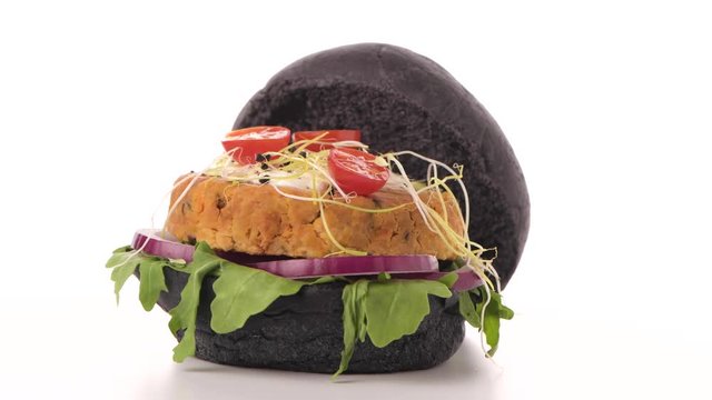 Tasty grilled veggie burger with chickpeas and vegetables on black bread on white background.