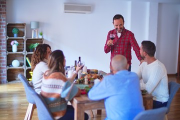 Beautiful family smiling happy and confident. Man speaking speech with cup of wine on hand celebrating Thanksgiving Day at home