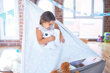 Adorable toddler sitting on the floor inside tipi around lots of toys at kindergarten