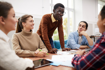 Large group of students working together on team project while studying in college, focus on smiling African-American man heading meeting